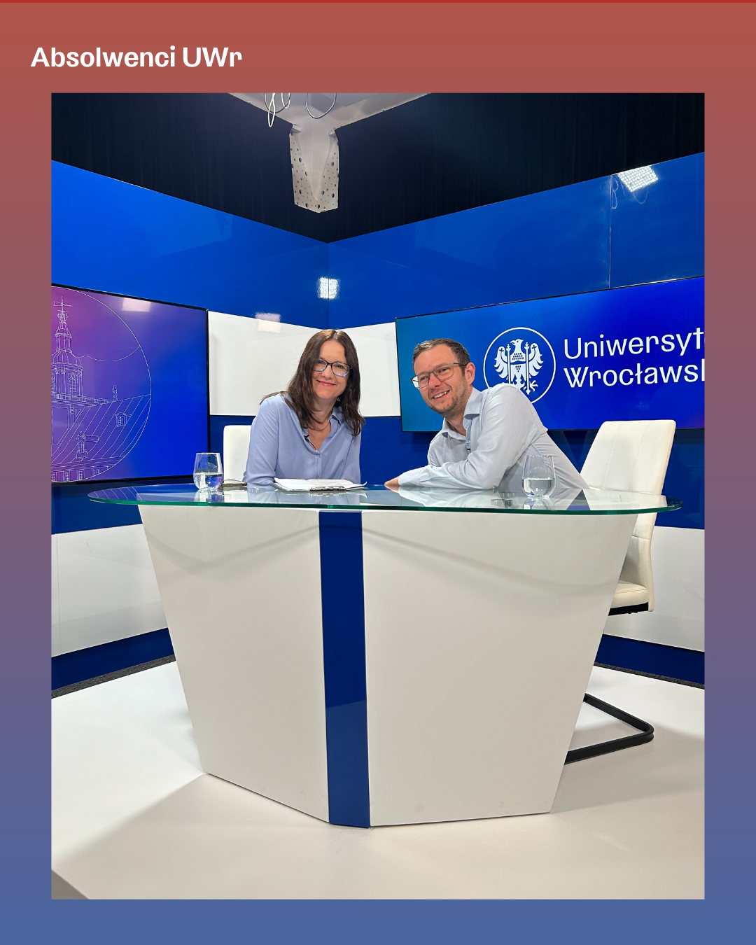 Zdjęcie przedstawia dwoje uczestników siedzących przy nowoczesnym, szklanym stole w studiu Uniwersytetu Wrocławskiego. Tło tworzą niebieskie panele i ekrany z grafikami oraz logo Uniwersytetu Wrocławskiego. Na stole stoją dwie szklanki z wodą oraz notatki. Studio jest jasno oświetlone, a nad stanowiskiem znajduje się zamocowany sprzęt oświetleniowy. Całość ujęta jest w ramce z gradientowym tłem, a w górnej części widnieje napis „Absolwenci UWr”.