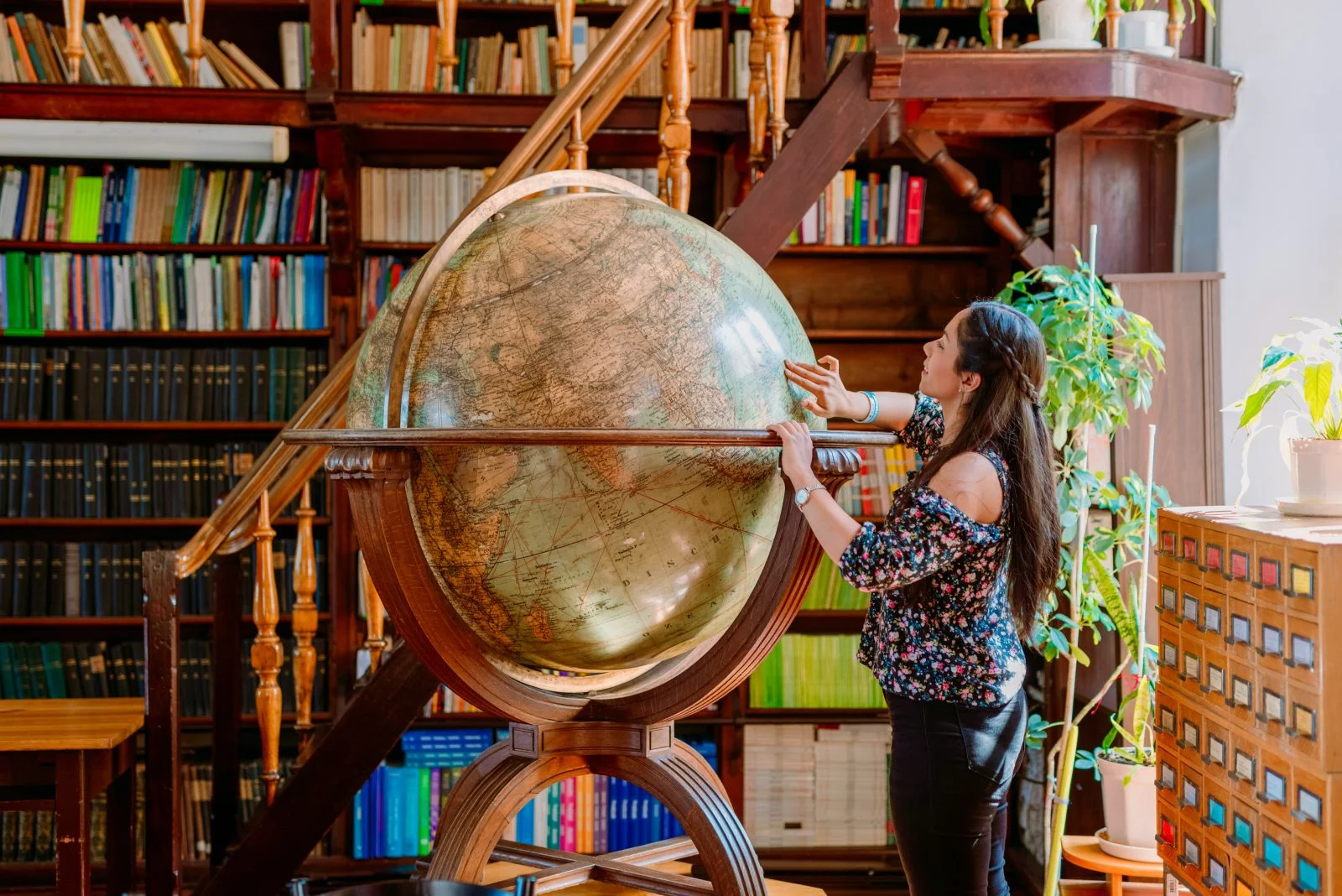 duży globus i kobieta przy nim, w tle schody i półki z książkami
