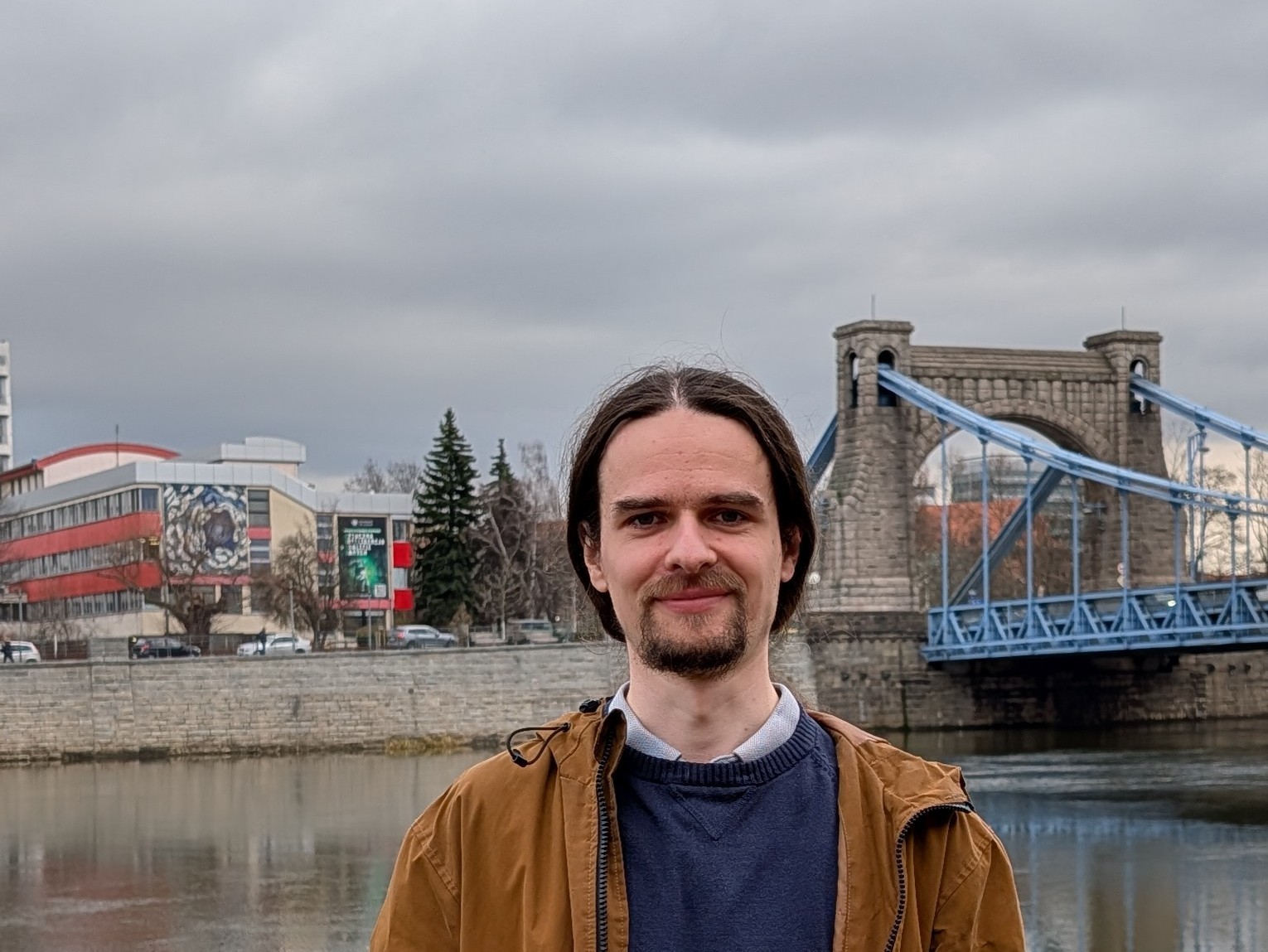 mężczyzna z długimi włosami na tle rzeki i mostu grunwaldzkiego