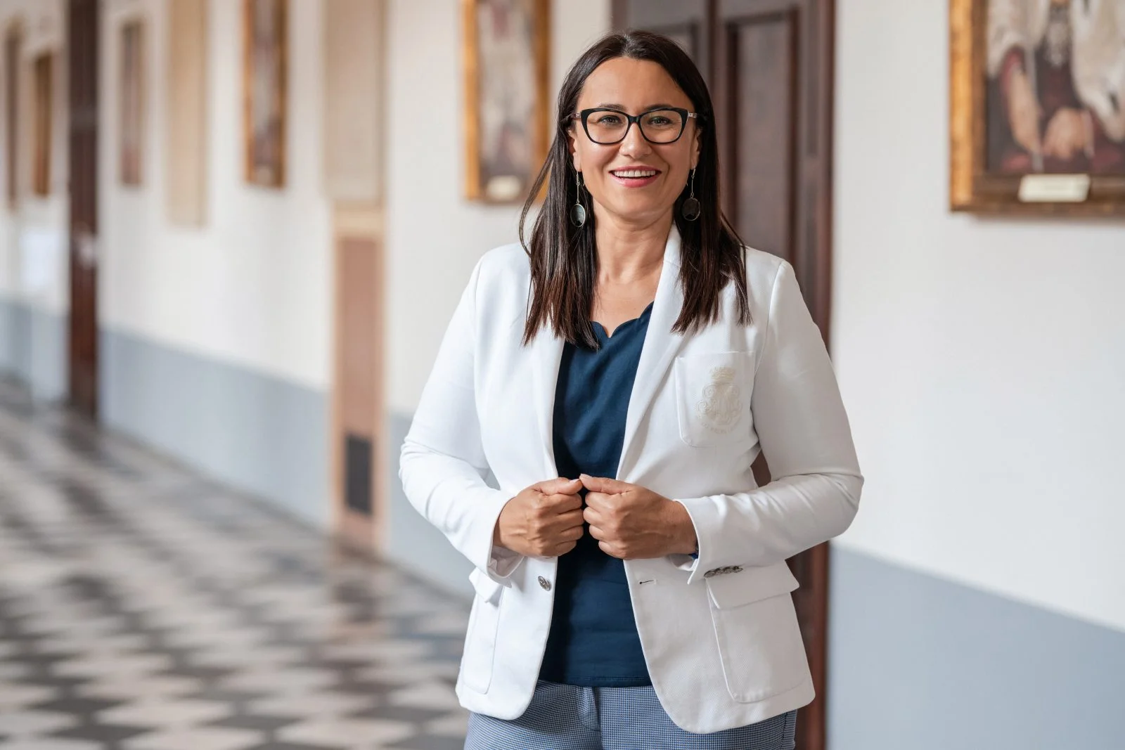 kobieta w marynarce uśmiecha się do kamery i stoi na korytarzu