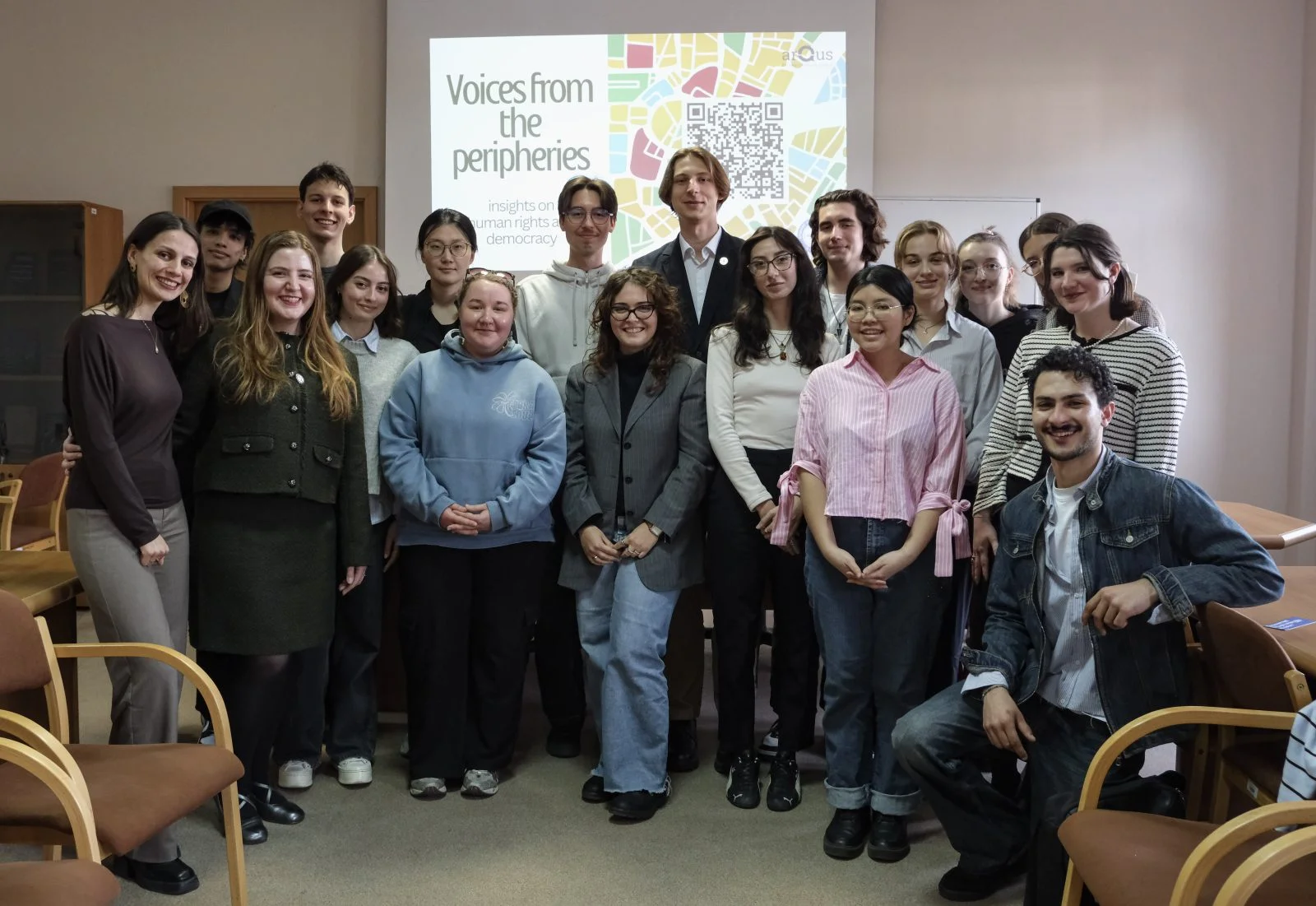 grupa ludzi pozująca do zdjęcia przed ekranem multimedialnym z napisem voices from the peripheries